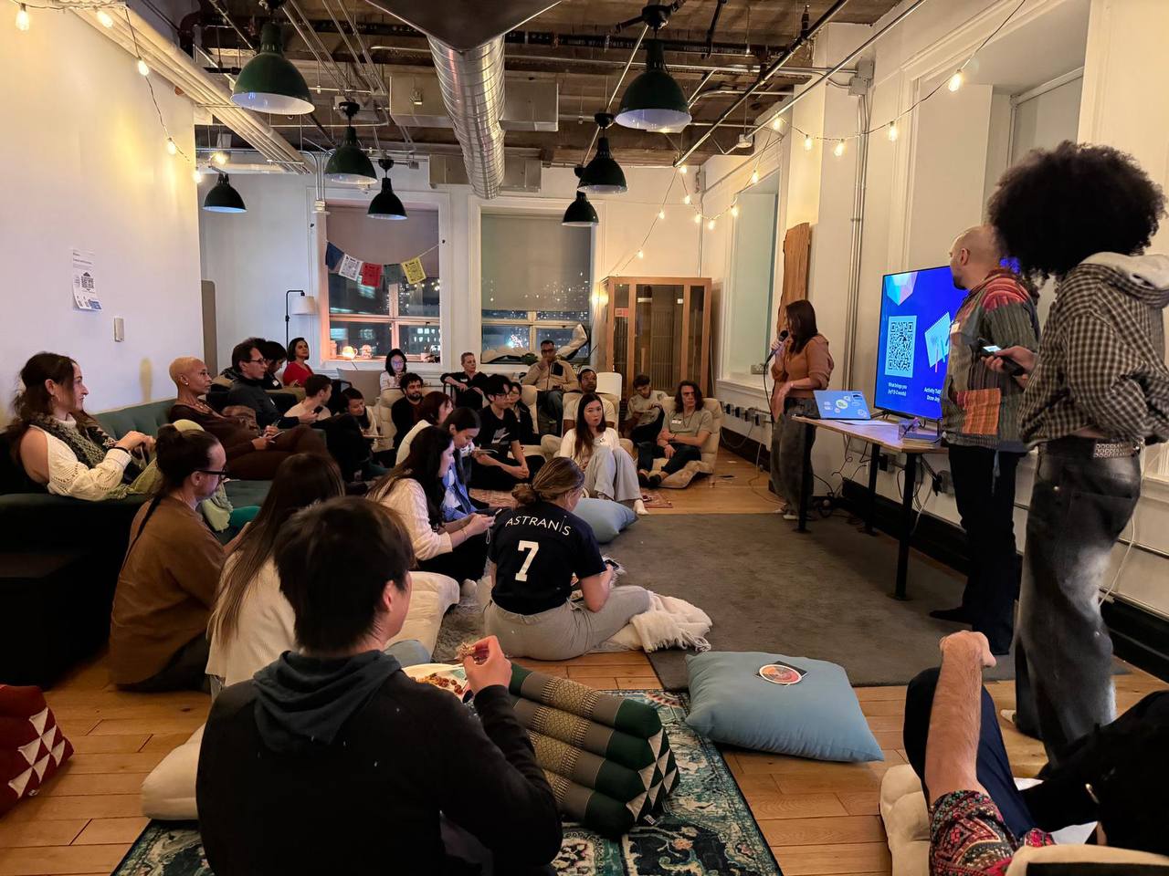 Community talk with speaker presenting to a packed room sitting on floor cushions